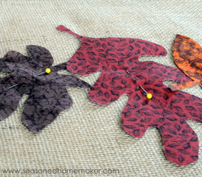 placing leaves on burlap table runner for Thanksgiving table decor